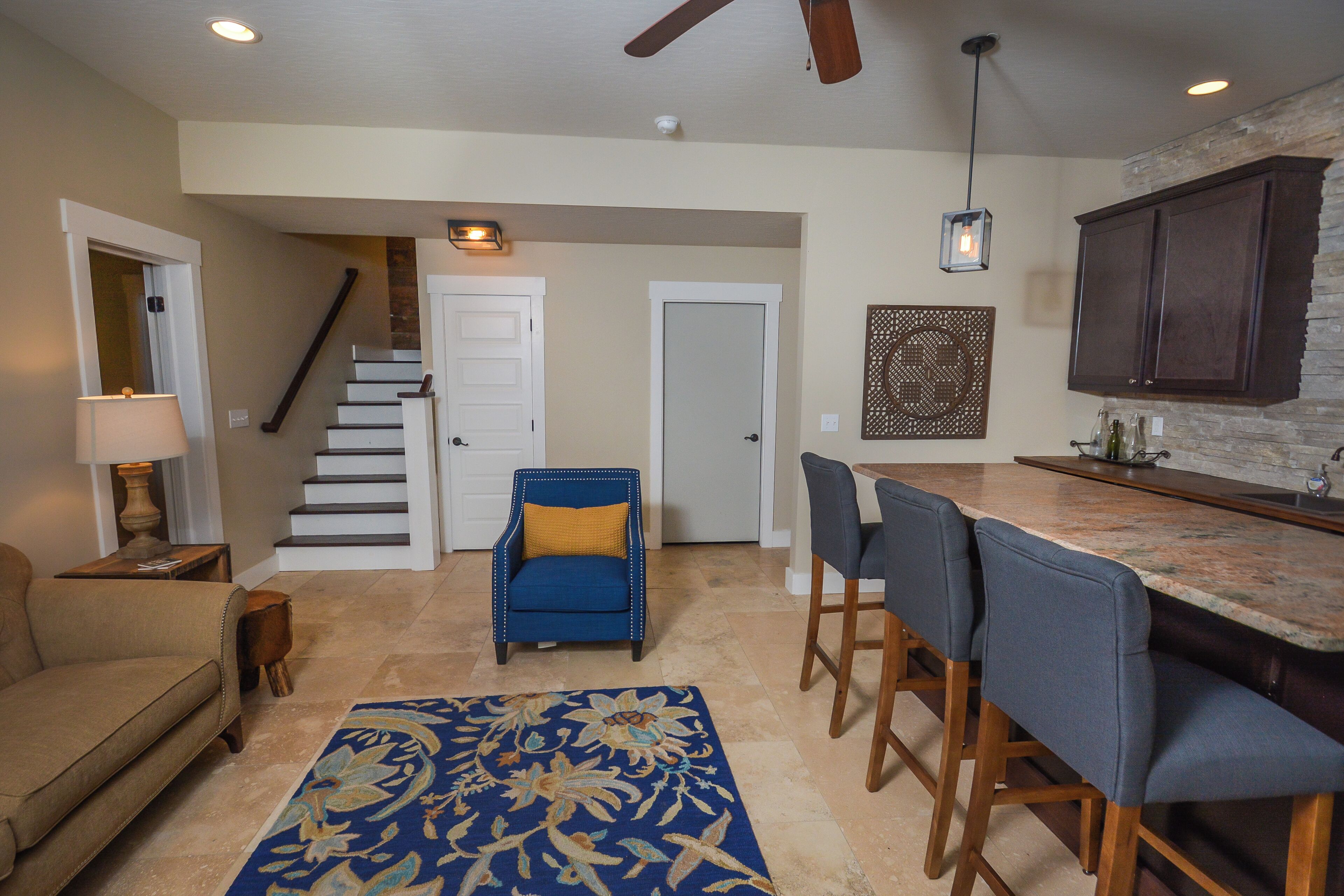 A spacious living room with a sofa, a blue armchair, a patterned rug, and a staircase leading to another level.