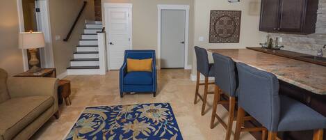 A spacious living room with a sofa, a blue armchair, a patterned rug, and a staircase leading to another level.