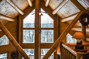 Cozy cabin-style interior with a high ceiling and large window offering a view of the surrounding landscape.