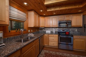 Enjoy a kitchen with cabinetry, granite countertops, stainless steel appliances, and a window overlooking the surrounding forest.