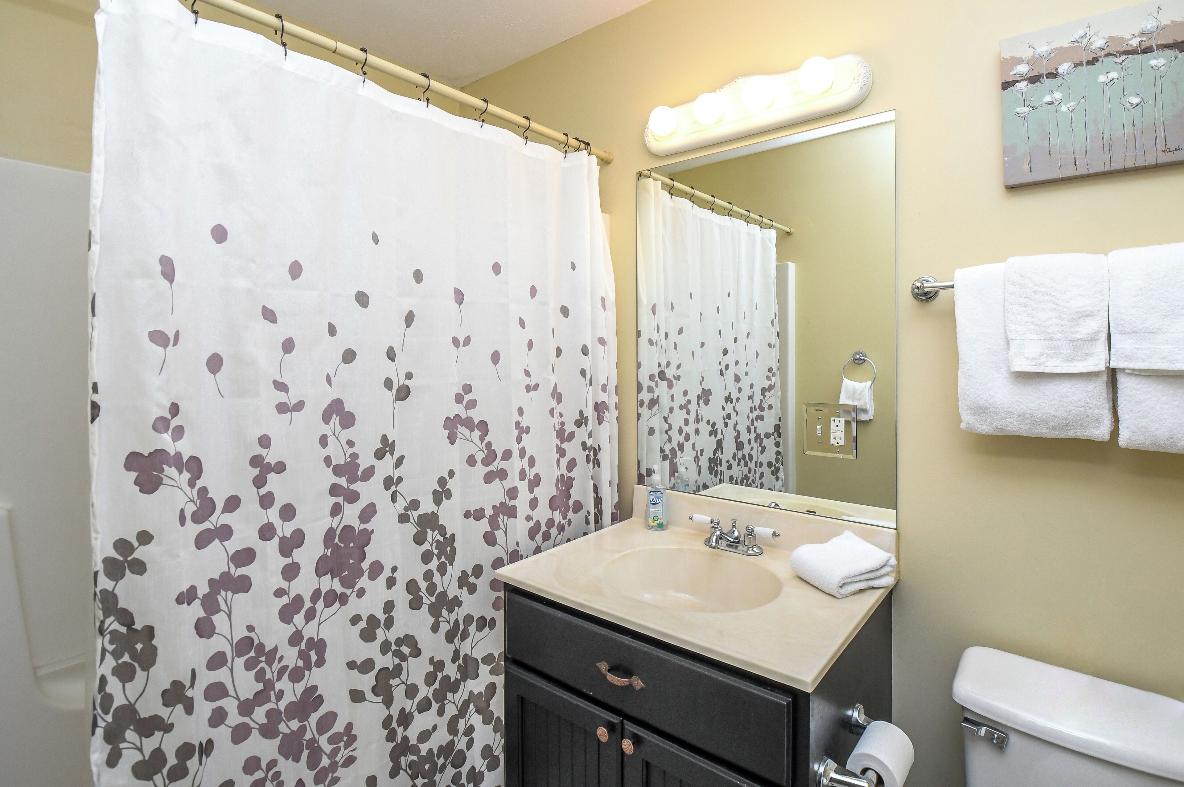 A bathroom with a shower curtain, sink, mirror, towel rack, and toilet.