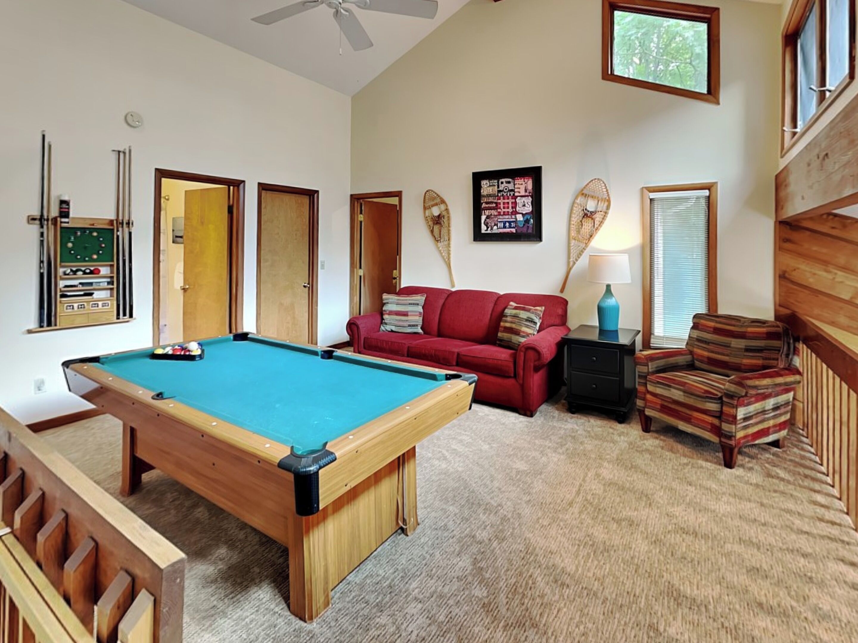 A pool table in a room with a red sofa, a striped armchair, and a lamp.