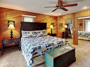 A bedroom with a wooden ceiling, a ceiling fan, a bed with a quilt, two bedside tables with lamps, a dresser, and a mirror.
