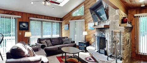 A cozy living room with a stone fireplace, a ceiling fan, and a large window.