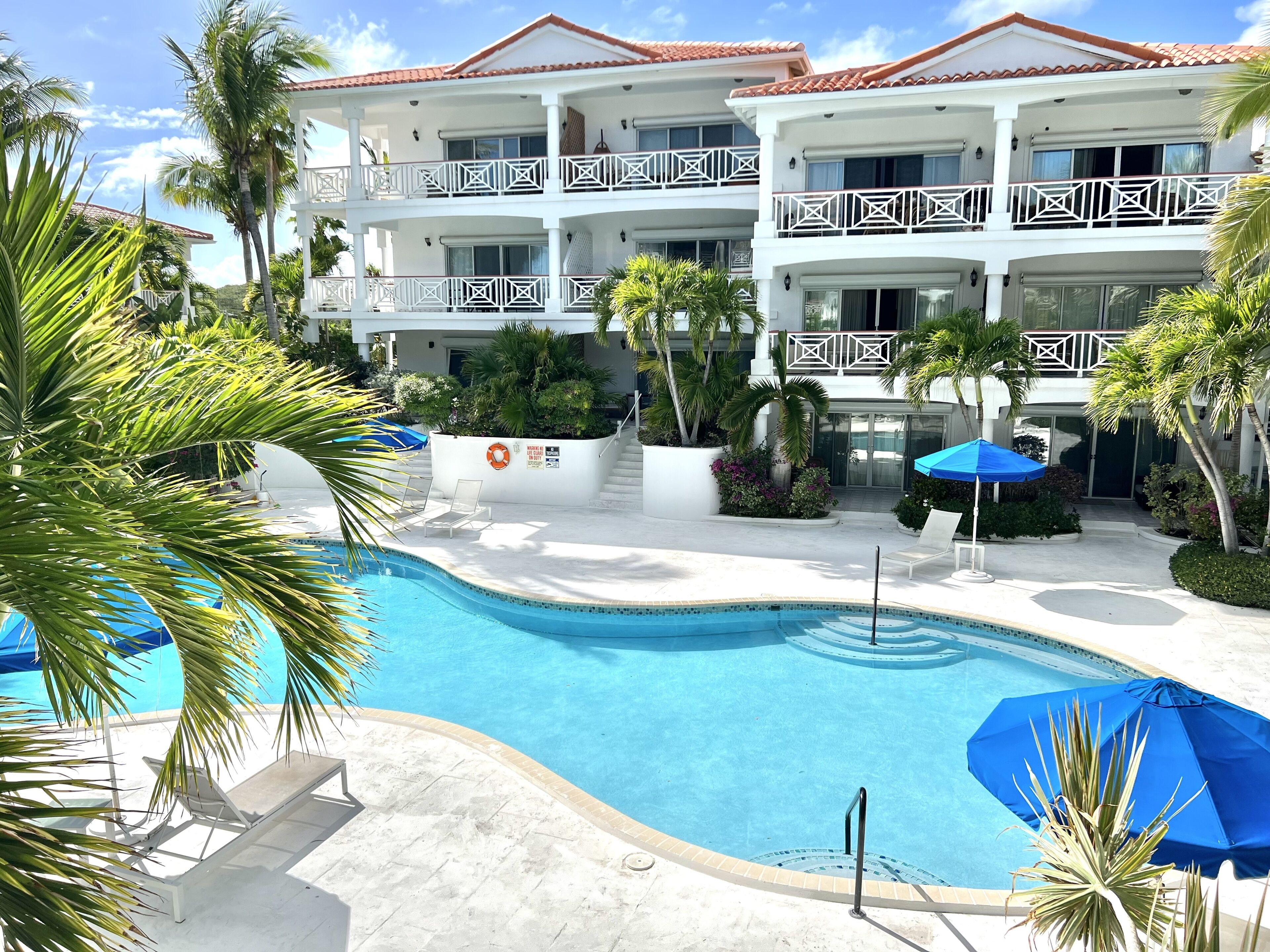 Een resort met een zwembad, witte balkons en palmbomen.
