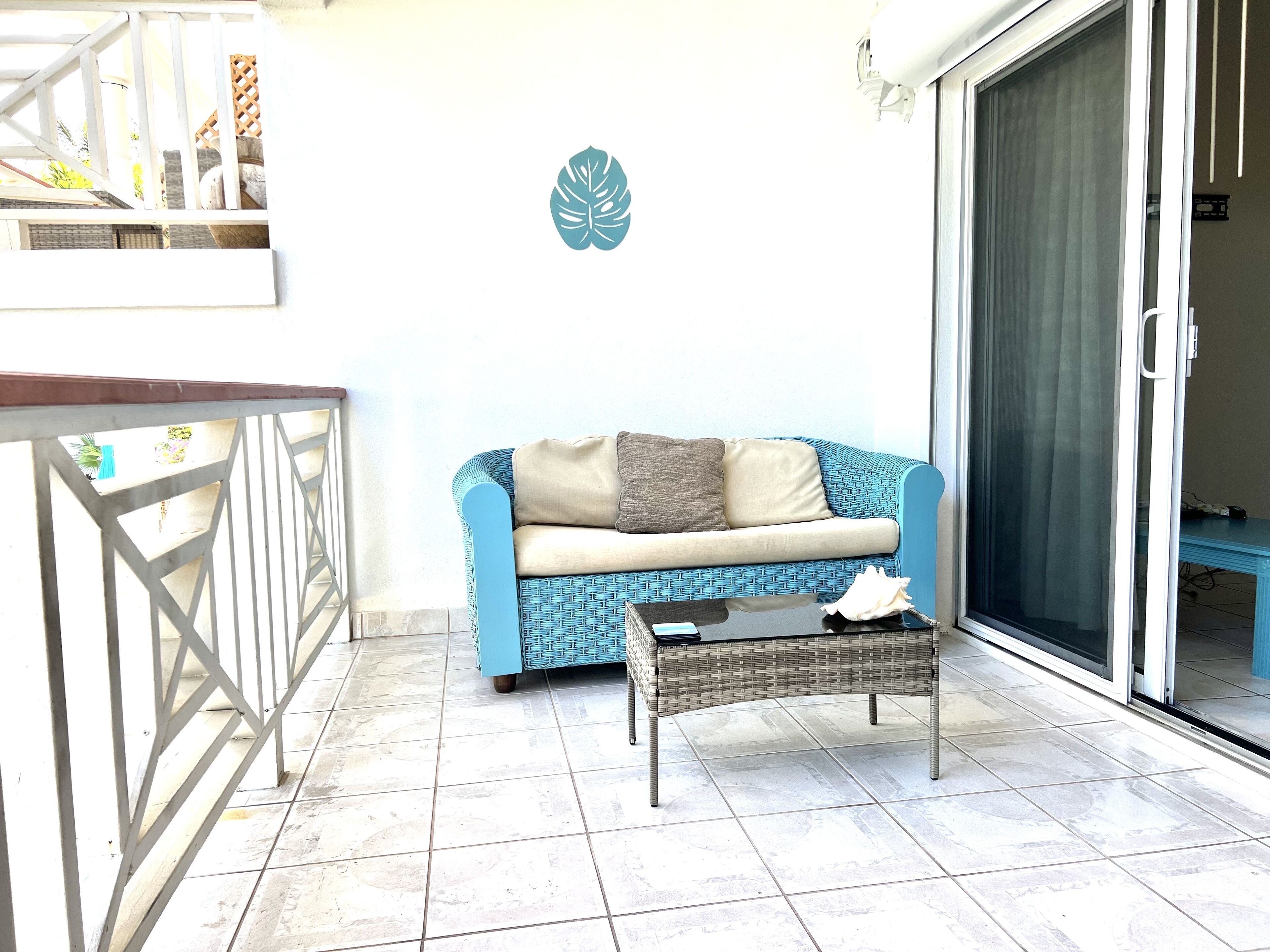 Un balcon avec un canapé bleu, une petite table et une décoration murale représentant des feuilles.