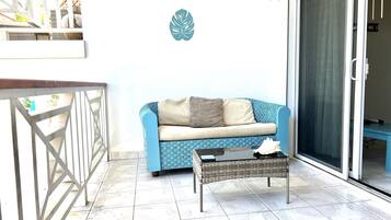 Un balcon avec un canapé bleu, une petite table et une décoration murale représentant des feuilles.