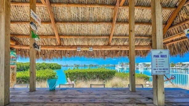 A wooden deck with a thatched roof overlooking a marina with boats.