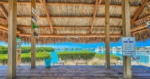 Une terrasse en bois, surmontée d’un toit de chaume, qui offre une vue sur une marina remplie de bateaux.