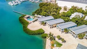 An aerial view of a coastal property with a swimming pool, a dock with boats, and a large building with a flat roof. - Sunset Pointe at Vaca Cove4 Bed 3 Baths, Saltwater Pool, Jacuzzi, Ocean View with Dock (Marathon)