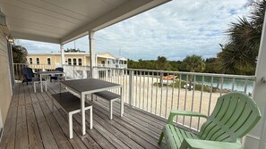 A wooden deck with a table and chairs, a covered area, and a view of the beach and ocean.