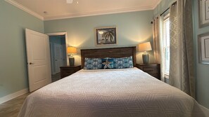 Un dormitorio con cama, dos mesitas de noche, una lámpara y un cuadro en la pared, además de una puerta.