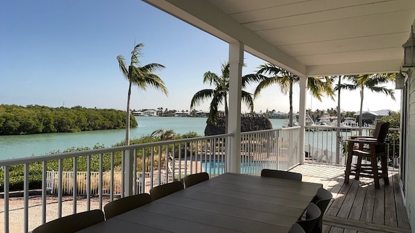 A covered outdoor area with a table and chairs, overlooking a body of water and a marina with boats.