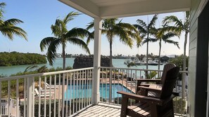A covered deck with a pool, palm trees, and a marina view.