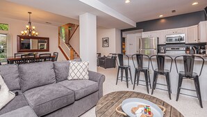 Un salon moderne avec un canapé gris, une table basse sur laquelle est posé un jeu de puzzle, et un escalier menant à un autre niveau.