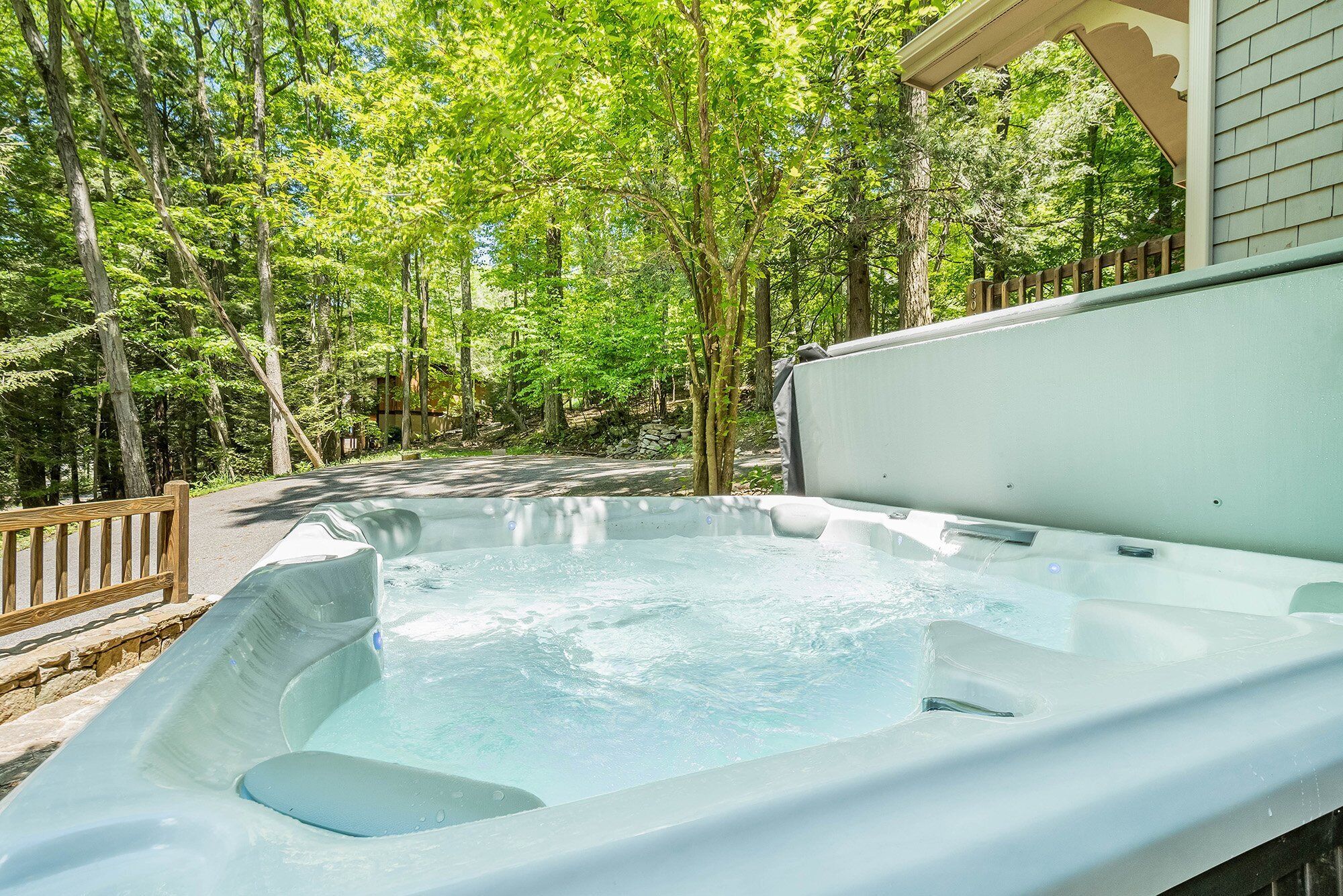 Un jacuzzi en un área boscosa con un muelle de madera y un muro de piedra al fondo.