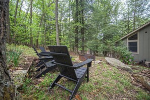 Un área boscosa con una cabaña pequeña y dos sillas Adirondack.