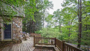 Une terrasse en bois avec des murs en pierre, des sièges d’extérieur et une vue sur la forêt environnante.