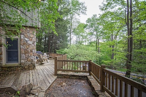 A wooden deck with stone walls, outdoor seating, and a view of the surrounding forest. - Cedars on the Rocks by Taylor Made Deep Creek (Oakland)