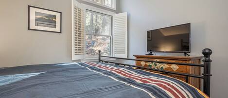 Un dormitorio con cama, cómoda, televisor y ventana con persianas.