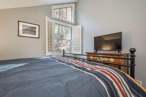 Un dormitorio con cama, cómoda, televisor y ventana con persianas.