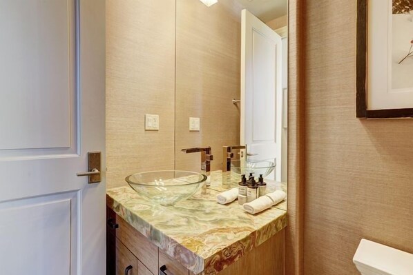 A bathroom with a glass bowl sink, wooden vanity, and a framed picture on the wall.