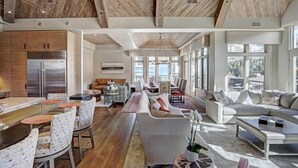 A spacious living area with a large sofa, dining table, and chairs. There is a kitchen with a refrigerator and cabinets. The room has large windows and a wooden ceiling. - Luxury Mountain-Side Penthouse with Stunning Views! by RedAwning (Vail)
