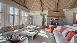A spacious living room with a high ceiling, large windows, and a stone fireplace. - Luxury Mountain-Side Penthouse with Stunning Views! by RedAwning (Vail)