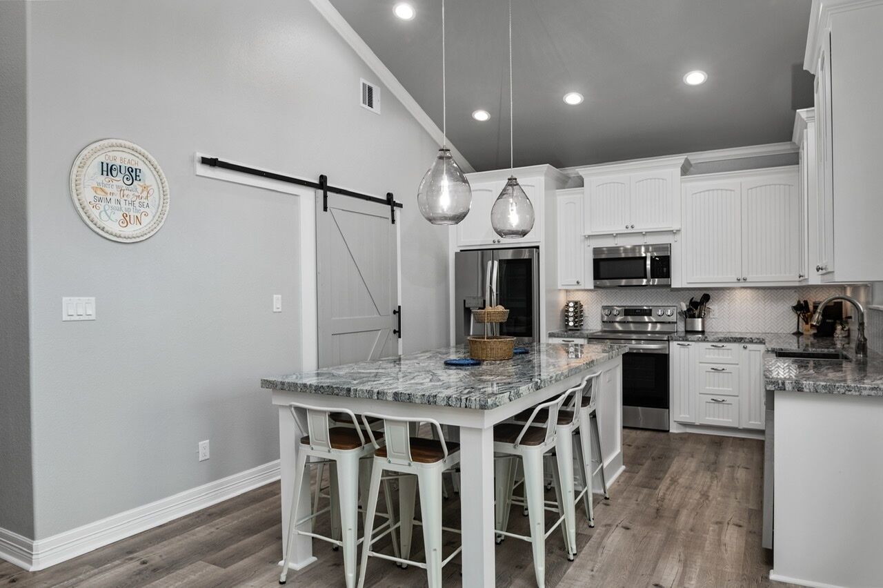 A kitchen with white cabinets, a marble island with bar stools, stainless steel appliances, and pendant lighting.