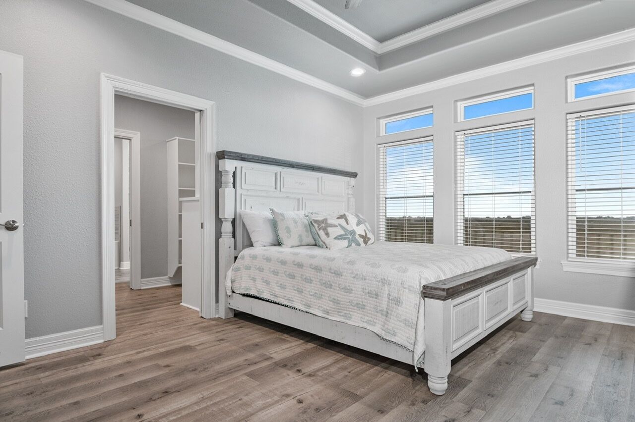 A bedroom with a white bed, wooden flooring, and a view through the window.