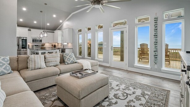 A spacious living room with a large sectional sofa, a ceiling fan, and a view of the outdoors through large windows.