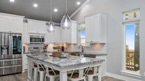 A modern kitchen with white cabinetry, stainless steel appliances, and a large island with bar stools.