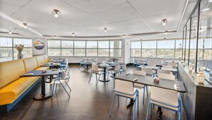 Uma sala de jantar moderna com mesas, cadeiras, janelas amplas e um banco amarelo.