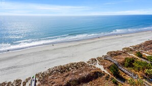 Uma praia com vista clara para o oceano, areal arenoso e um calçadão que leva à praia.