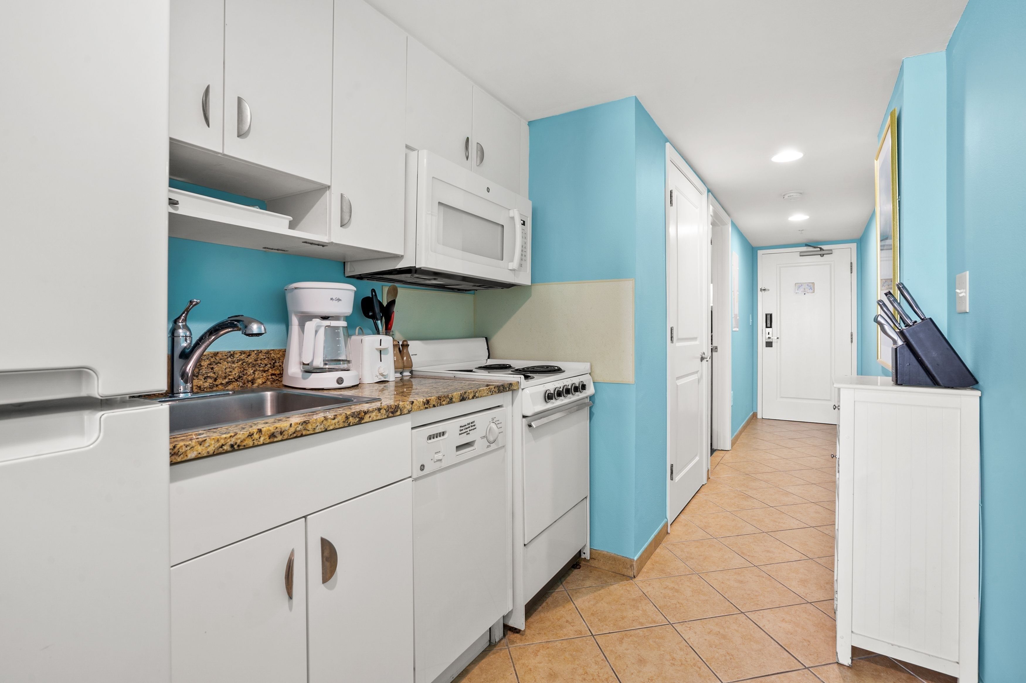 A kitchen with white cabinets, a microwave, a coffee maker, and a stove.