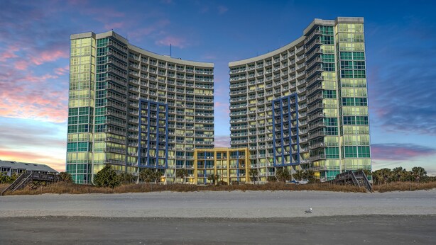 Um hotel moderno e imponente com átrio central, várias varandas e vista para a praia.