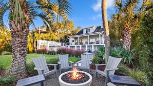 Ein Feuerkorb mit Sitzgelegenheiten in einem Gartenbereich, umgeben von Palmen und einem Haus im Hintergrund.