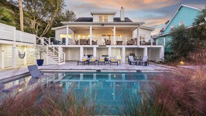 Ein zweigeschossiges Haus mit Pool, Sitzgelegenheiten im Freien und einer überdachten Terrasse.