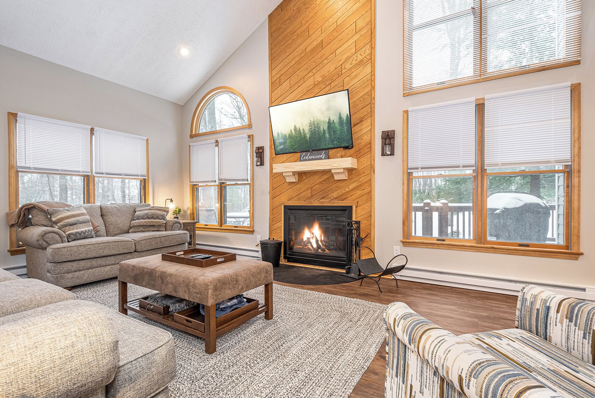 A cozy living room with a fireplace, large windows, and a comfortable seating area.