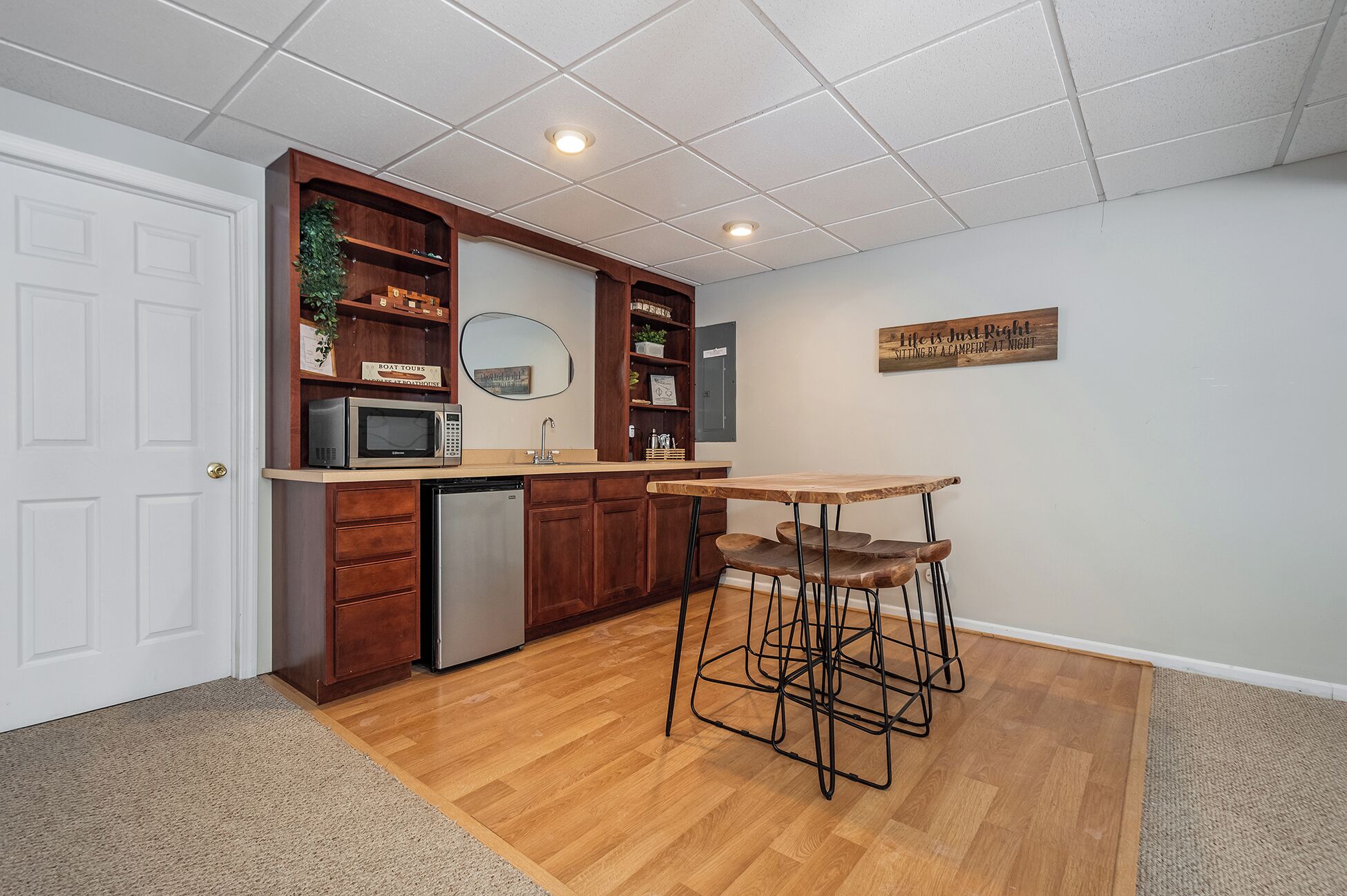 A compact kitchen with wooden cabinets, a microwave, a refrigerator, and a bar stool.