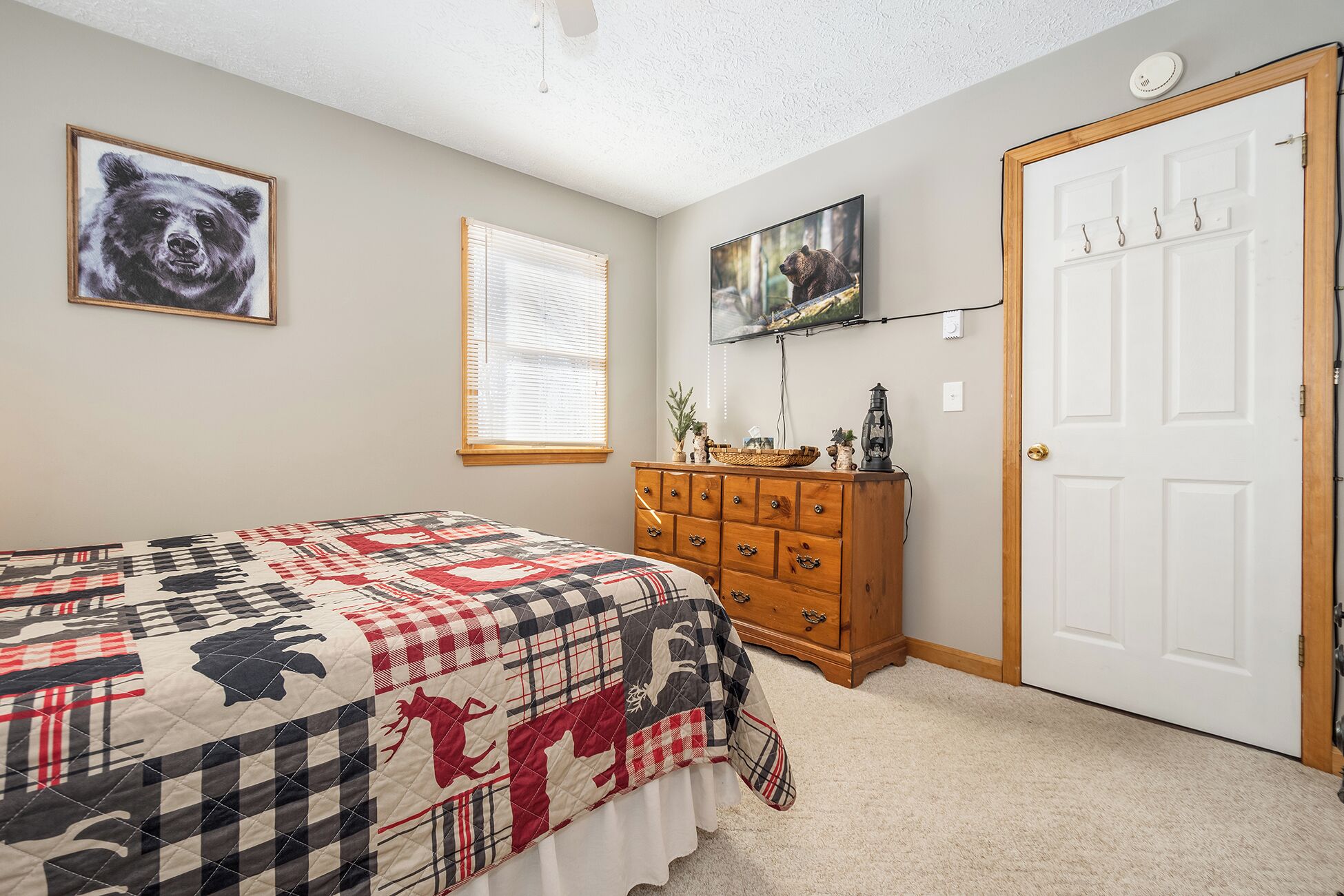 A bedroom with a bed, a dresser, a door, and two wall-mounted pictures.