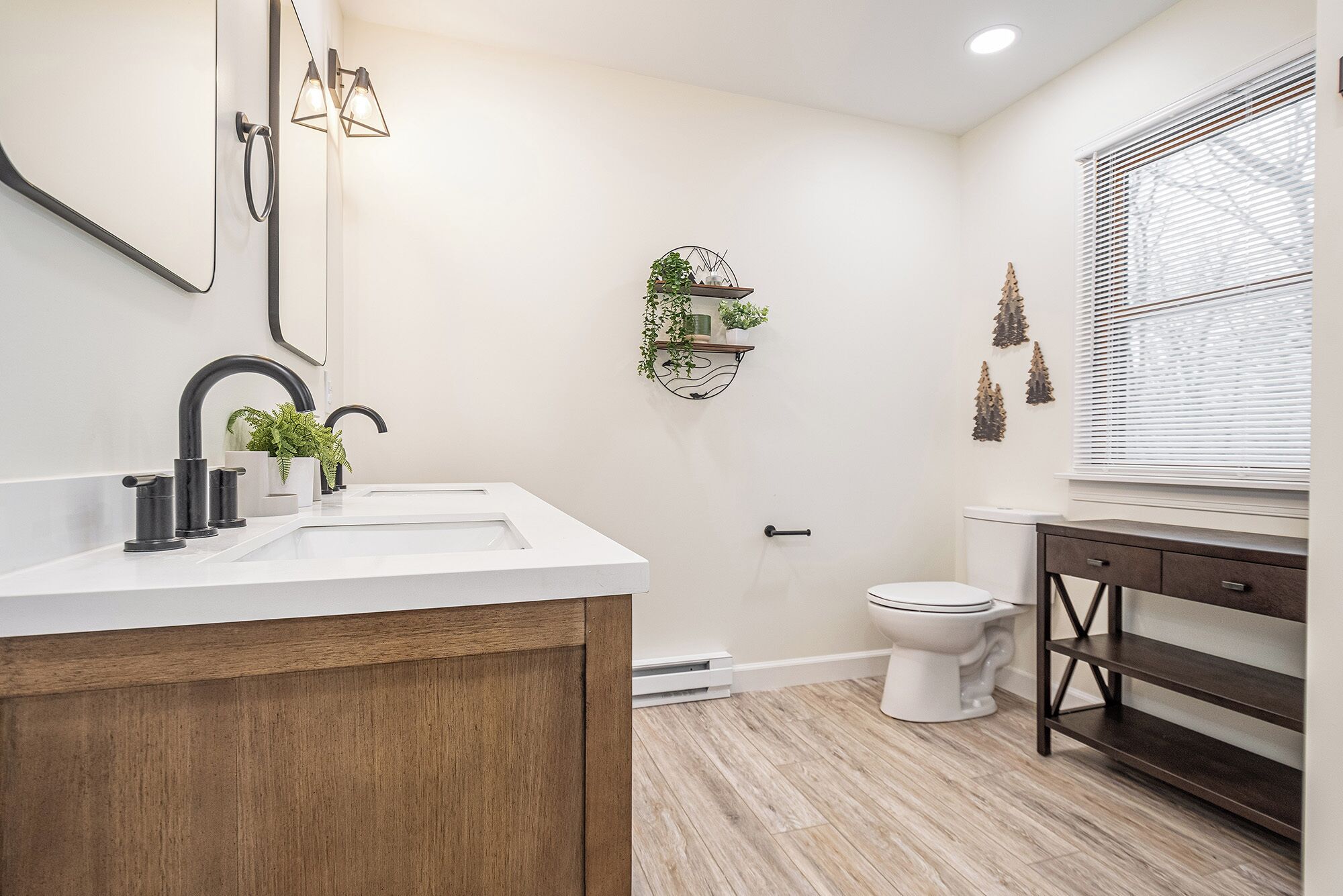 Une salle de bain moderne avec un lavabo blanc, un robinet noir et un meuble-lavabo en bois. On y trouve également des toilettes et une fenêtre avec des stores.