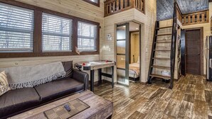 Interior acogedor de una cabaña con piso de madera, un sofá, una mesa y un altillo accesible por una escalera.