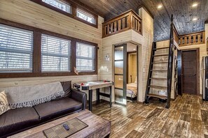 A cabin interior with a loft bedroom, a dining area, and a living room with a sofa and table.