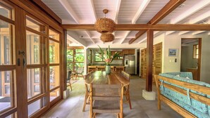 A spacious dining area with a wooden table and chairs, a woven ceiling light, and large windows.
