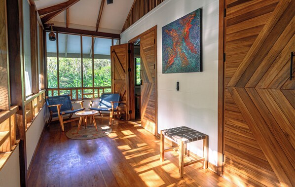 A wooden interior with a large window, a blue chair, a small table, and a wooden bench.