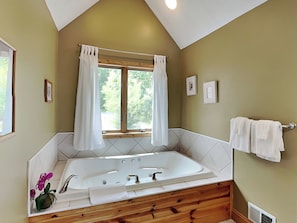 A bathroom with a freestanding bathtub, wooden vanity, two windows with curtains, and a towel rack. - Celebration at Deep Creek by Taylor Made Deep Creek (Oakland)