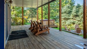 A covered deck with wooden chairs and a hot tub. - Celebration at Deep Creek by Taylor Made Deep Creek (Oakland)