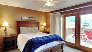 A bedroom with a bed, two bedside tables with lamps, a ceiling fan, and a sliding glass door leading to an outdoor area with red chairs. - Celebration at Deep Creek by Taylor Made Deep Creek (Oakland)