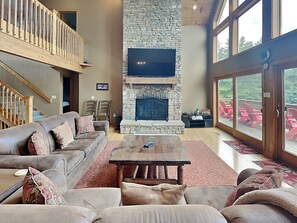 A spacious living room with a stone fireplace, a large flat-screen TV, a wooden coffee table, and a comfortable seating area. - Celebration at Deep Creek by Taylor Made Deep Creek (Oakland)